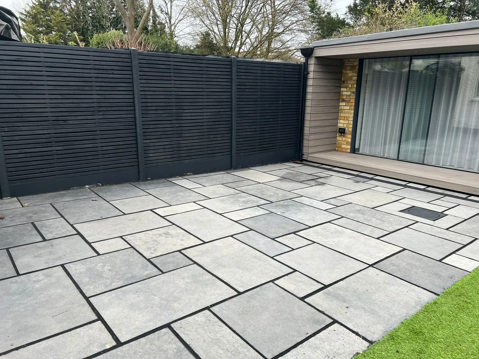 Stone-paved London courtyard with new dark slatted fencing and a glass-and-brick rear extension