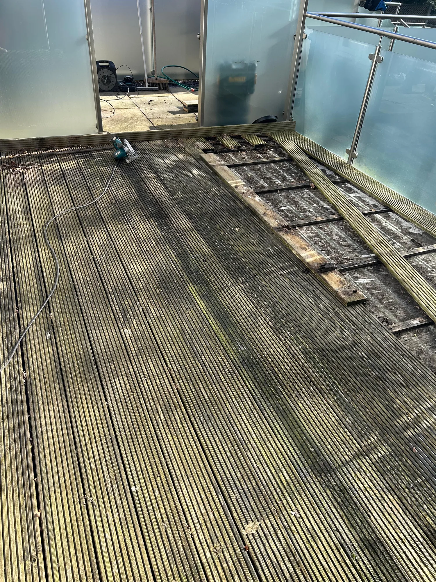 Before: rotted timber decking with moss and missing boards on a glass-balustrade terrace