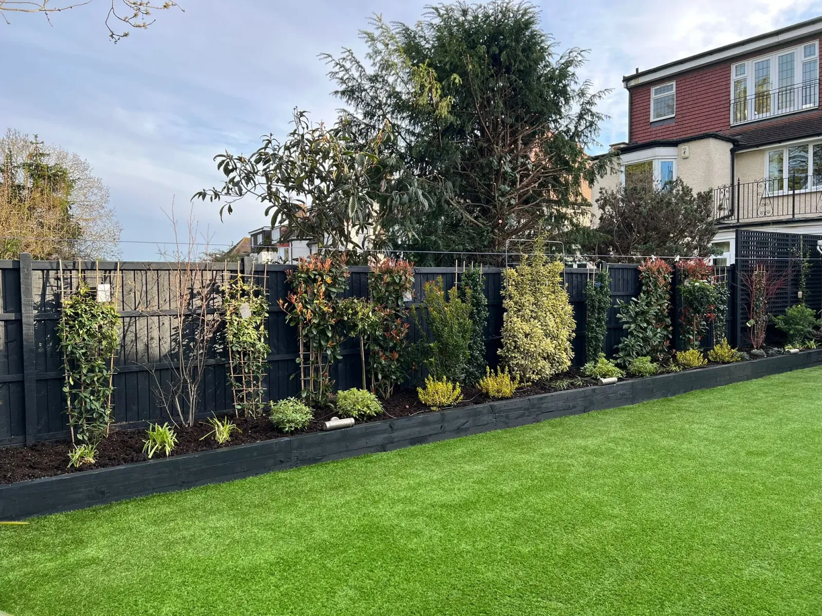 After: newly planted variegated shrubs and photinia in the black sleeper raised bed